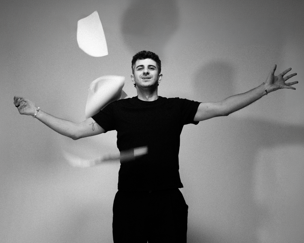 Man i svart t-shirt kastar papper i luften mot neutral bakgrund